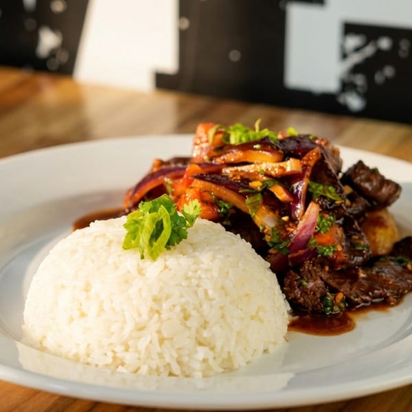 A white plate holds a mound of white rice and saucy beef with red onions and herbs.